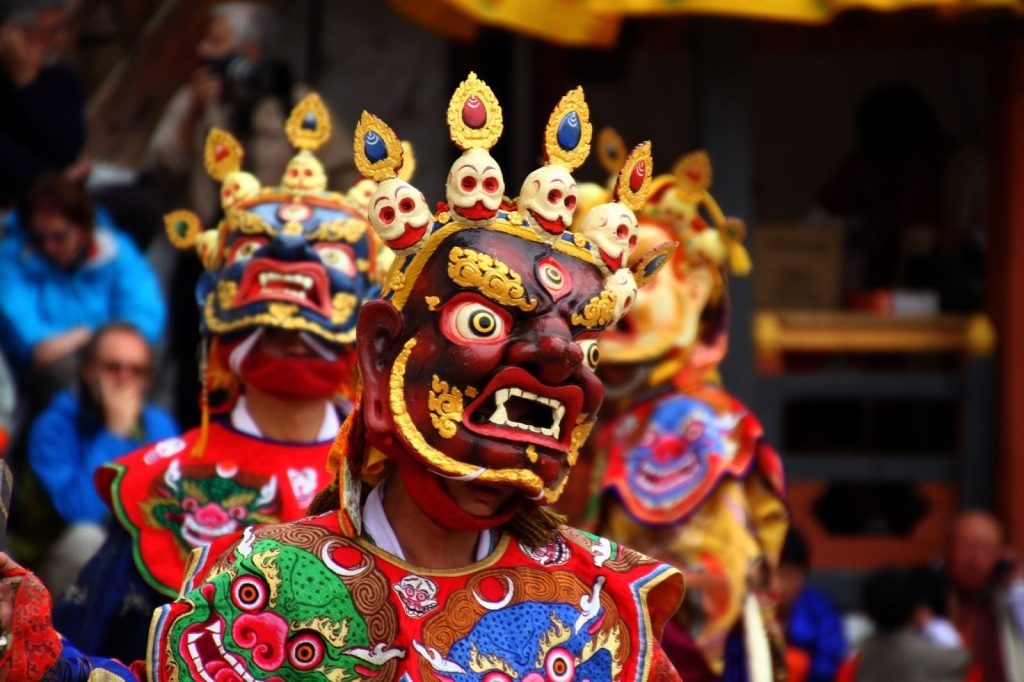  Bhutanese dancers in elaborate traditional masks and robes performing a sacred cham dance during a cultural festival, representing Bhutan’s cultural preservation and Gross National Happiness values.
