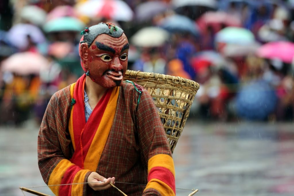 Bhutanese man wearing a traditional festival mask during a cultural celebration, showcasing Bhutan’s heritage and the values of Gross National Happiness.