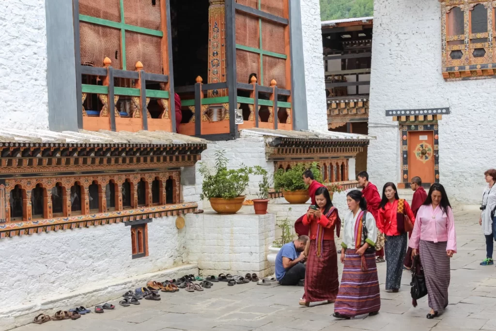 Bhutanese women in traditional kira dress walking outside a monastery in Bhutan, reflecting cultural preservation, environmental conservation in Bhutan, and sustainable tourism.